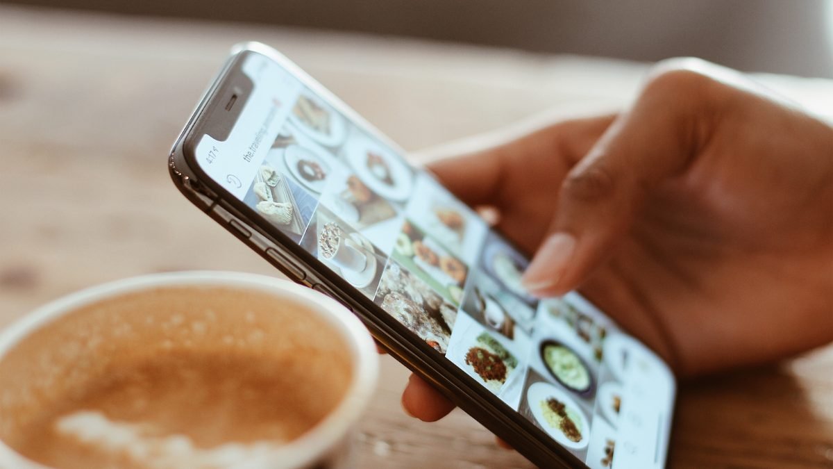 Mão segurando um celular navegando pelo feed do Instagram